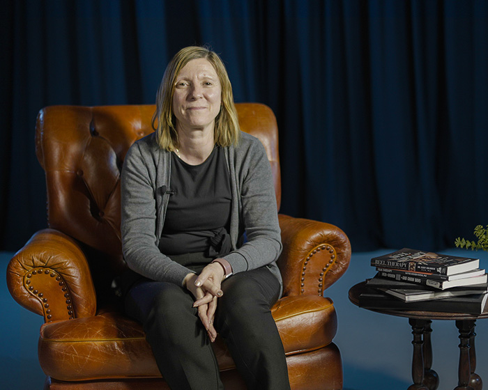 A woman sat in an armchair next to a table of books smiling